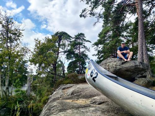 a man sitting on a rock next to a boat at Boafall Lodge in Jämshög