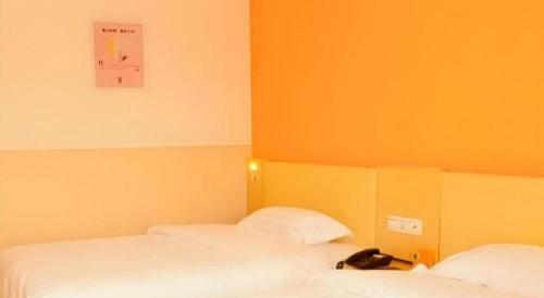 two beds in a room with orange walls at 7 Days Inn Guangrao Bus Station in Dongying