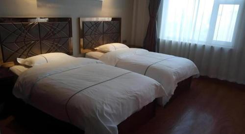 two beds in a hotel room with white sheets at GreenTree Inn Geermu Walking Street Business Hotel in Golmud