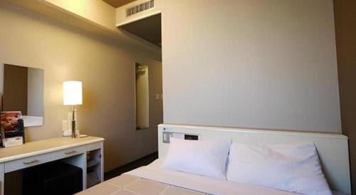 a bedroom with a bed and a desk with a lamp at Hotel Route Inn Kitamatsudo Ekimae in Kashiwa