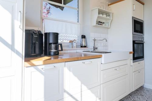 a white kitchen with white cabinets and a window at Reethaus MeerFerien direkt am Wasser in Mellnitz