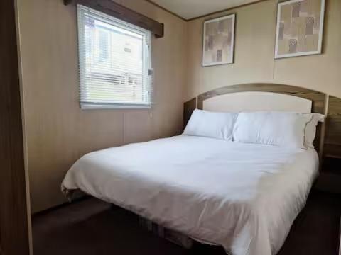 巴德利索尔特顿Elms Caravan with sea views at Devon Cliffs的卧室里有一张铺着白色床单的床和一扇窗户