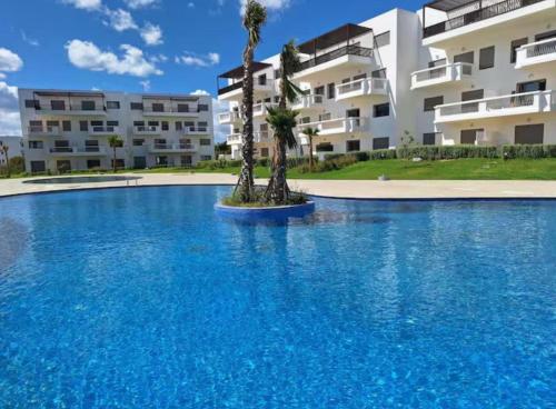 a large swimming pool with palm trees in front of a building at Escapade chic & cosy à Cabo in Cabo Negro