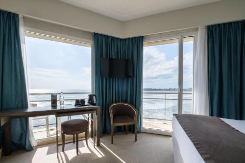a hotel room with a bed and a desk and windows at Hotel & Spa Les Roches Noires in Les Sables-dʼOlonne