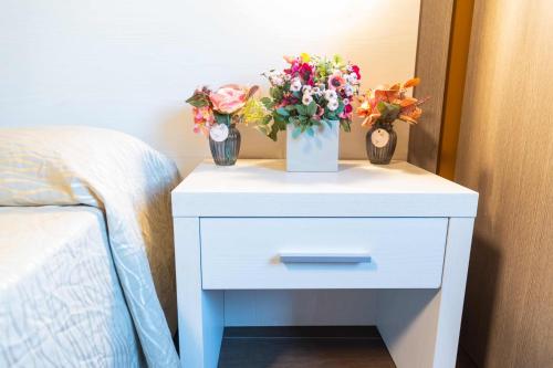 a white bedside table with two vases of flowers on it at Ferrari Hotel in Carugate