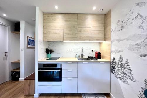 une cuisine avec des placards blancs et une fresque murale représentant la montagne. dans l'établissement Cosy 30m in the heart of Combloux, à Combloux