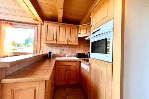 La cuisine est équipée de placards en bois, d'un évier et d'un four micro-ondes. dans l'établissement Apartment with balcony at the gates of Megève, à Combloux