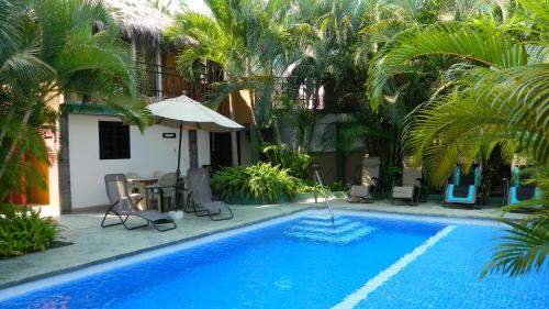 a pool with chairs and an umbrella and palm trees at Hotel Condominium La Posada de Bucerias in Bucerías