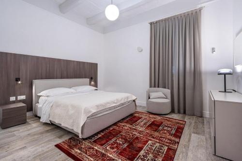a white bedroom with a large bed and a chair at Old Theatre Suites - Elba in Valletta