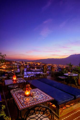 a rooftop patio with tables and chairs at night at Riad Bab Mahrouk in Chefchaouene