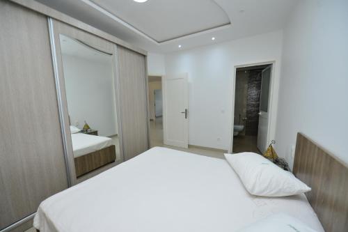 a bedroom with a white bed and a mirror at Dar Hella Apartments in El Maamoura