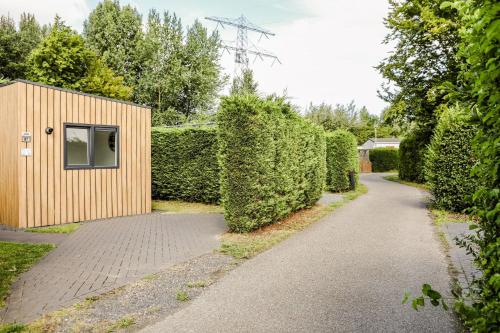 a path next to a hedge with a building at Stijlvol Tiny House Zeeland - Centraal gelegen VP022 in Heinkensand