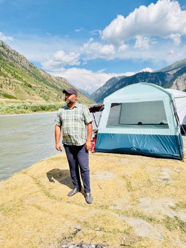 a man standing next to a tent next to a lake at Sea Green Guest House in Srinagar