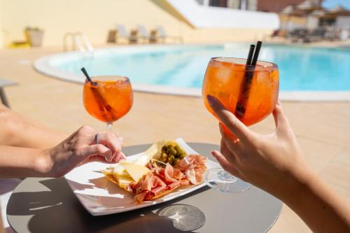 two people sitting at a table with a plate of food and two drinks at Felix Hotels - Hotel La Baja in Santa Caterina