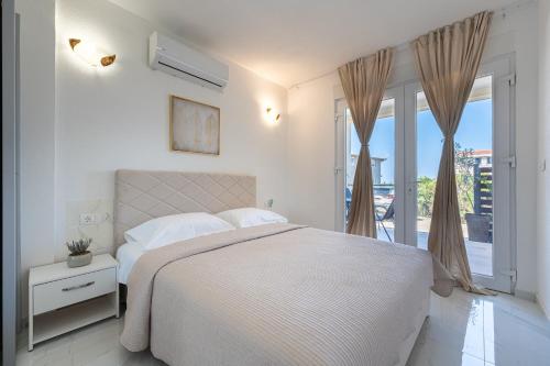 a white bedroom with a bed and a balcony at OliveRock Apartments - Hladna Uvala in Kruče