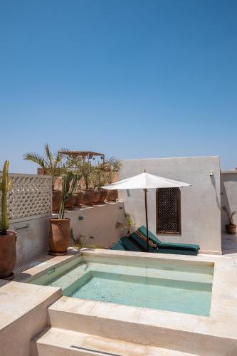 a swimming pool with an umbrella next to a house at Alrashid Marrakech Boutique Hotel & SPA in Marrakech