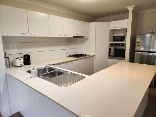 a white kitchen with a sink and a counter at Simple and Comfy Family Home between BNE and Ipswich in Bellbird Park