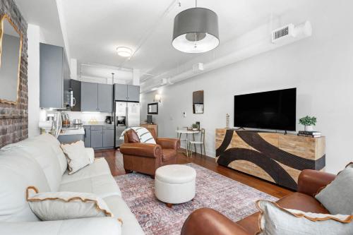 a living room with white furniture and a flat screen tv at Lush Savannah Loft - Near Plant Riverside District in Savannah