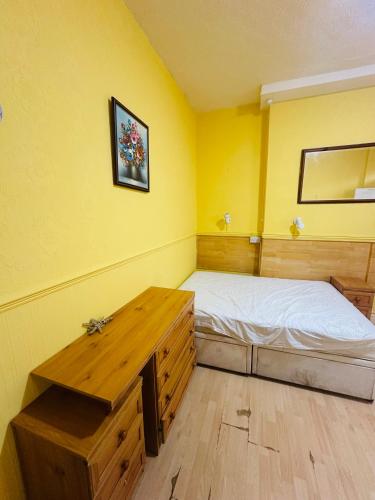 een gele kamer met een bed en een houten tafel bij Saxonia guest house in Weston-super-Mare