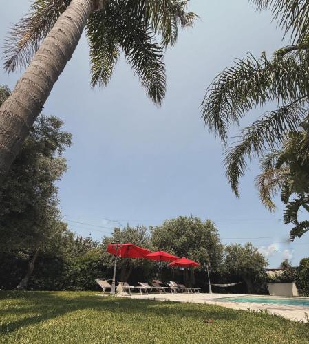 a pool with tables and red umbrellas in a park at Amati home in Floridia