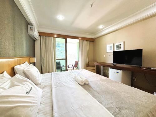 Un dormitorio con una gran cama blanca y un televisor de pantalla plana. en Apartamento com Estrutura de Hotel na Barra, en Río de Janeiro