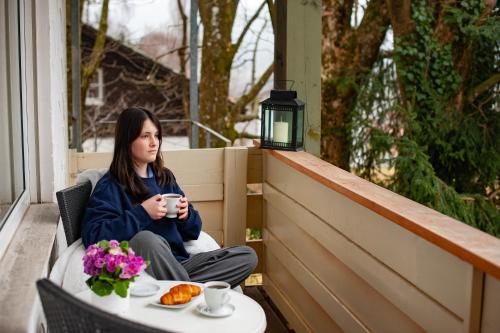 a woman sitting on a porch with a cup of coffee at LuCA Hotel in Bodenmais