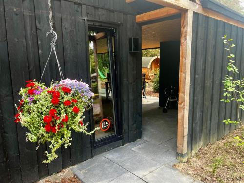 a black building with a hanging basket of flowers at Wellness in the Woods - 4p TinyHouse met privé sauna & hottub in Diessen