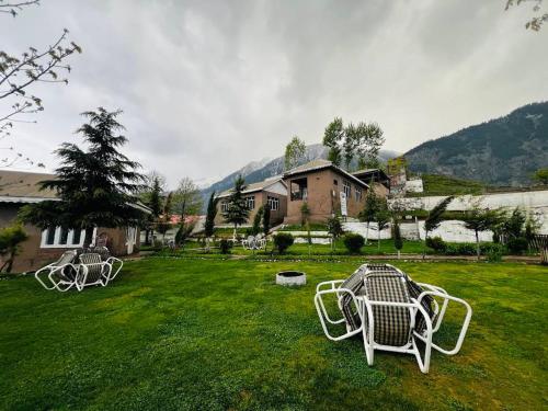 two white chairs in a yard with a house at Forest Valley Cottages Kalam by Khan Familia Travels in Kalām