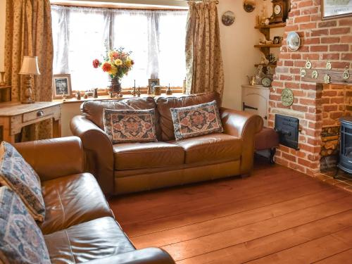 a living room with a leather couch and a brick wall at Honeysuckle Cottage in Great Yarmouth
