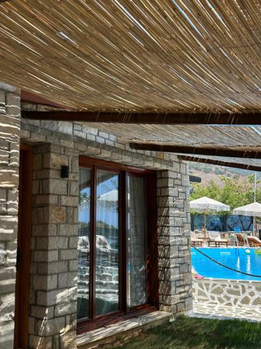 a stone house with a pool and a wooden roof at Palermiti Luxury Rooms in Himare