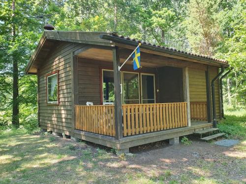 a small cabin with a porch and a flag on it at Cozy cottage with its own beach plot and rowing boat in Linneryd