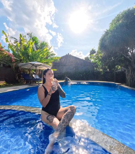 a woman sitting in a swimming pool drinking a drink at Suka Sari Cottages in Pemuteran