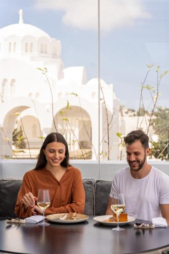 a man and woman sitting at a table with wine glasses at Aressana Spa Hotel & Suites - Small Luxury Hotels of the World in Fira