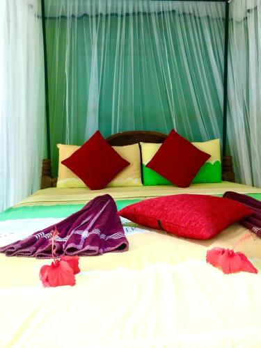 a bed with red and green pillows on it at Green Bamboo House in Sigiriya