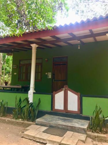 a green house with a door and a porch at Green Bamboo House in Sigiriya