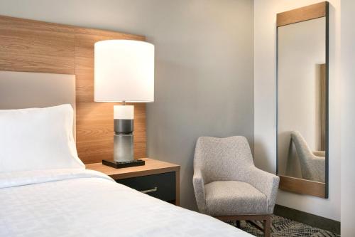 a bedroom with a bed and a chair and a mirror at Candlewood Suites Wake Forest-Raleigh Area by IHG in Wake Forest