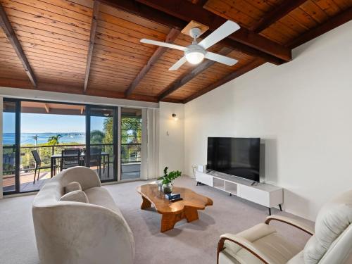 a living room with a ceiling fan and a flat screen tv at Coastal Family Escape with Pool Balcony and Bay Views in Ormiston