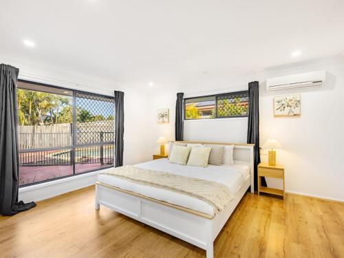 a white bedroom with a bed and a large window at Spacious Home 4BR Retreat with Pool in Parkinson in Browns Plains