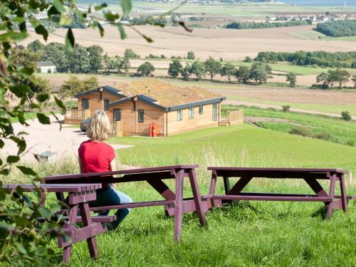 a woman sitting on a picnic table in front of a house at 3 Bed in St Andrews 88420 in Balmullo