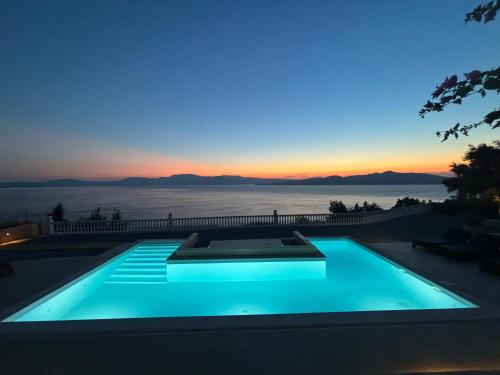 a blue swimming pool with a sunset in the background at Trabala Ionian Living in Paleros