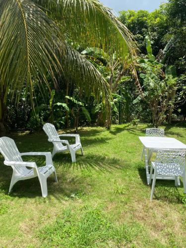three white chairs and a table in the grass at Maison charmante à Baie-Mahault avec jardin clôturé in Baie-Mahault