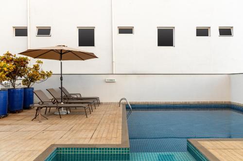 a pool with chairs and an umbrella next to a table with an umbrella at Araçatuba Plaza Hotel in Araçatuba