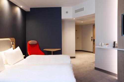 a hotel room with a bed and a red chair at Holiday Inn Express & Suites Monheim am Rhein by IHG in Monheim