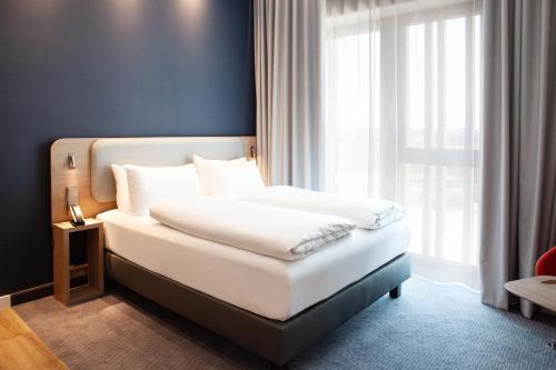 a bedroom with a white bed with a window at Holiday Inn Express & Suites Monheim am Rhein by IHG in Monheim