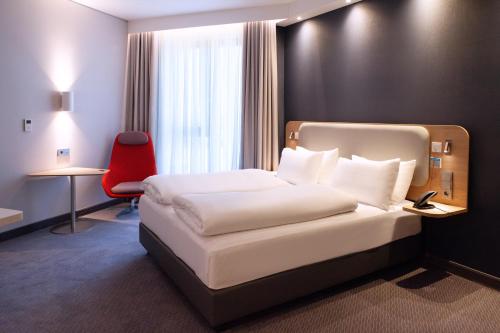 a hotel room with a bed and a red chair at Holiday Inn Express & Suites Monheim am Rhein by IHG in Monheim