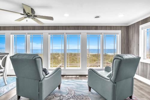 a living room with two chairs and large windows at Reelaxing in Oak Island