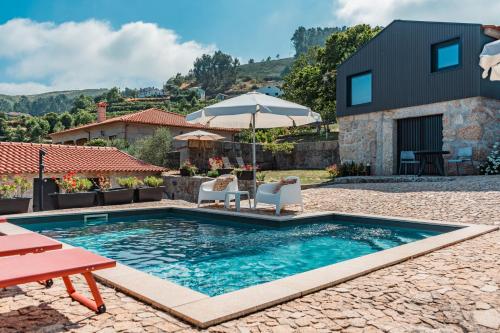 a swimming pool with two chairs and an umbrella at Villa Seara - Casas da Vinha in Celorico de Basto