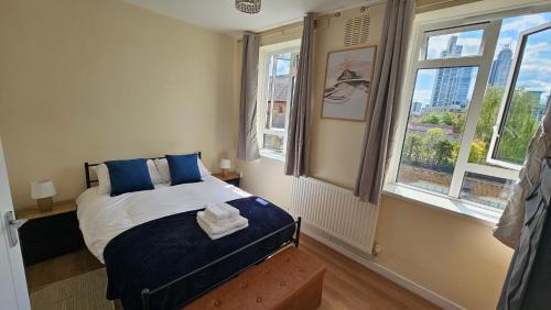 a bedroom with a bed with blue pillows and two windows at Cozy Vauxhall Nest-3 bedroom flat, with balcony and lift in London