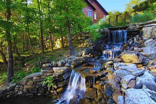 a stone wall with a waterfall in front of a house at Stonewater Cove in Shell Knob