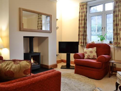 a living room with a fireplace and two chairs and a mirror at Rose Cottage in Betws-y-coed